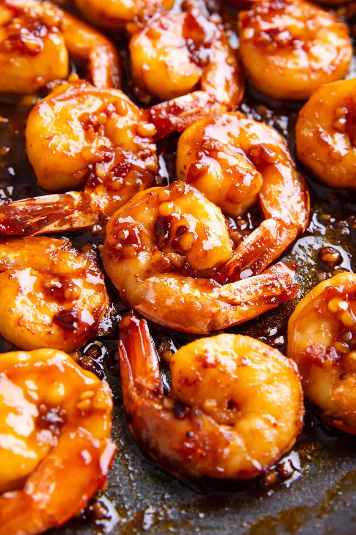 Eine Nahaufnahme von asiatischen Knoblauchgarnelen, bedeckt mit einer würzigen und süßen asiatischen Sauce, die mit gehacktem Knoblauch, Ingwer, Sriracha, Chiliöl und Sesamöl angereichert ist.