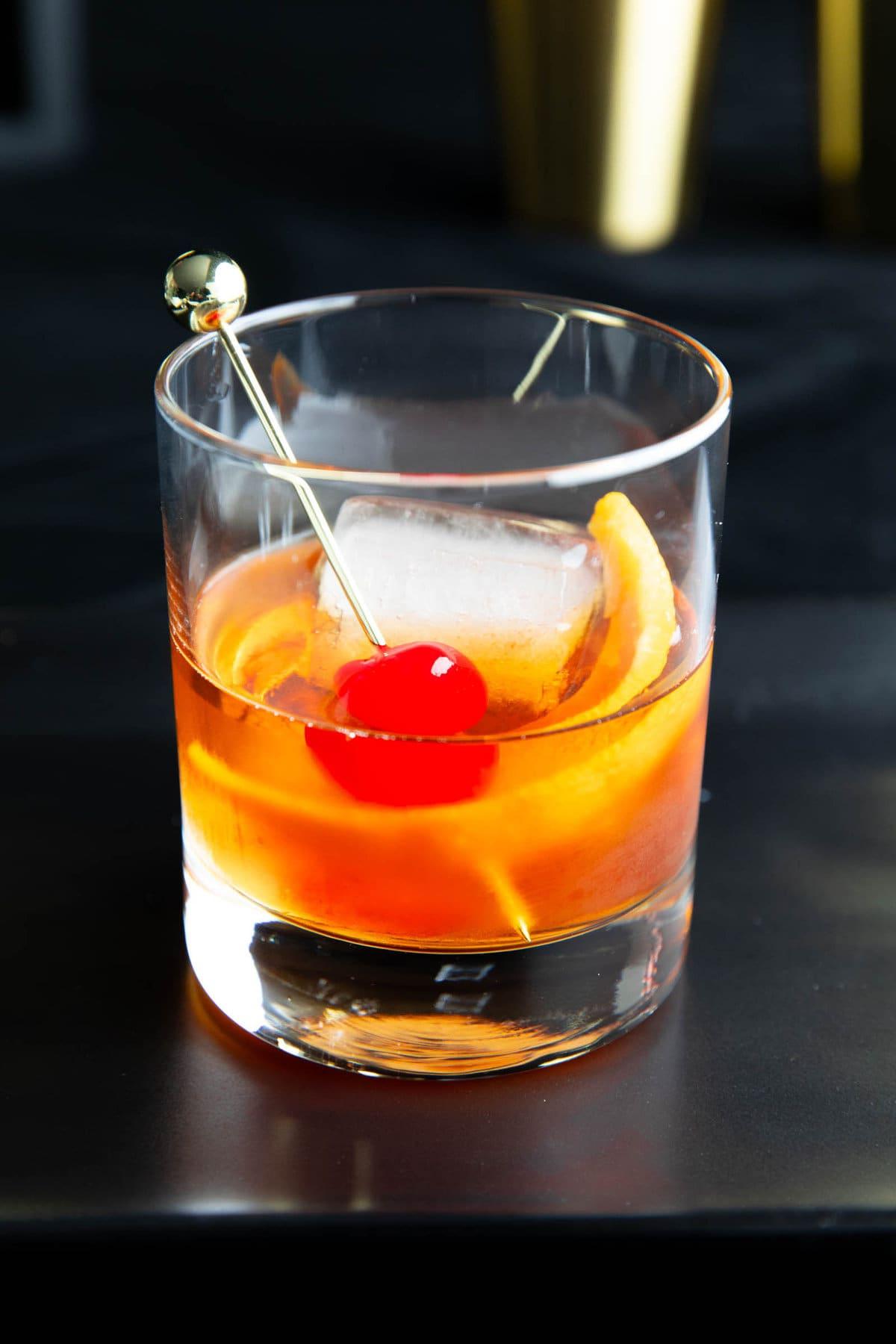 Old Fashioned Getränkerezept 2 Ein Old Fashioned Whiskey-Cocktail, garniert mit Orangenzeste und einer Maraschino-Kirsche, nahaufnahme