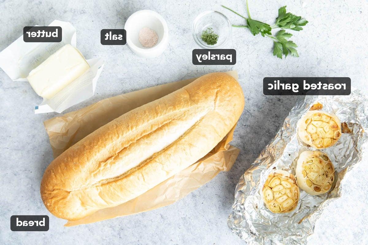 Geröstetes Knoblauchbrot {Hausgemachtes Rezept} 3 Zutaten für geröstetes Knoblauchbrot, darunter ein Brotlaib, Butter, Salz, gerösteter Knoblauch und Petersilie auf einem Küchentisch