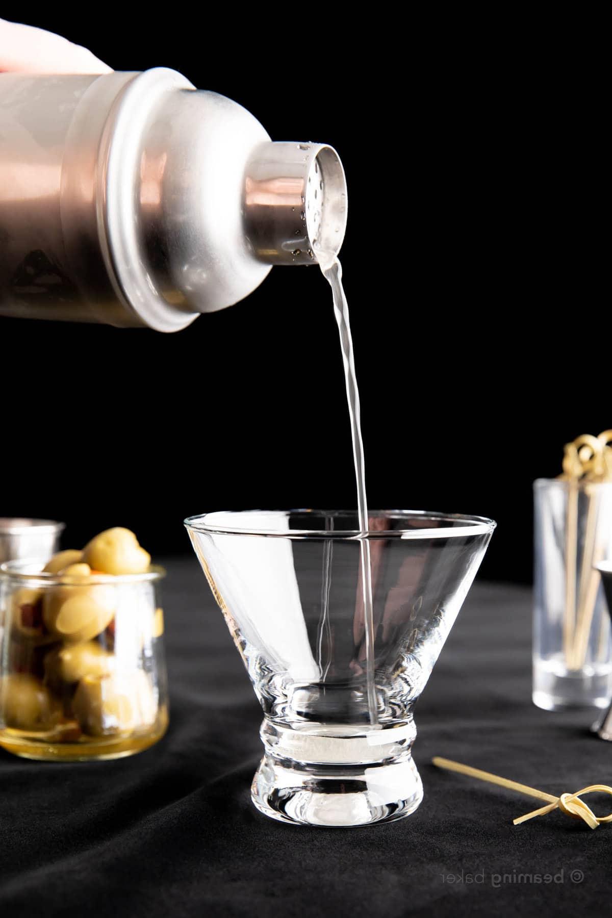 Extra Schmutziger Martini 4 Eine Hand, die Flüssigkeit aus einem Edelstahl-Cocktailshaker in ein Martini-Glas gießt