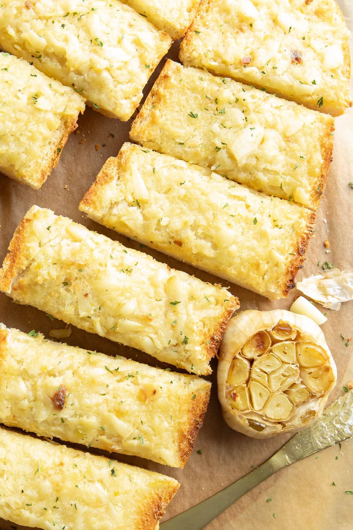 Geröstetes Knoblauchbrot {Hausgemachtes Rezept} 4 Knoblauchbrotscheiben auf einem Serviertablett mit einem Kopf geröstetem Knoblauch und einem Streichmesser