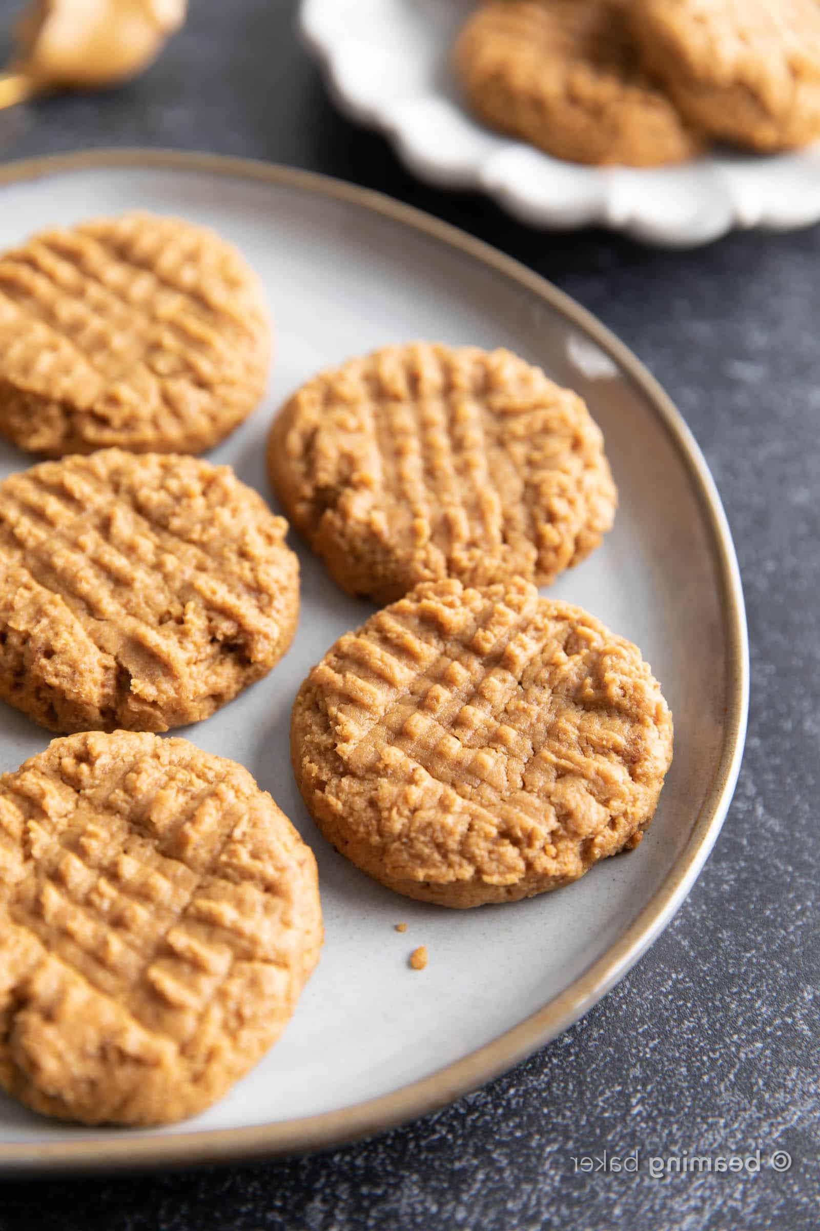 Gesunde Erdnussbutterkekse mit nur 4 Zutaten 4 Auf einem dunklen Tisch liegen Erdnussbutter-Kekse auf einem Teller verteilt.