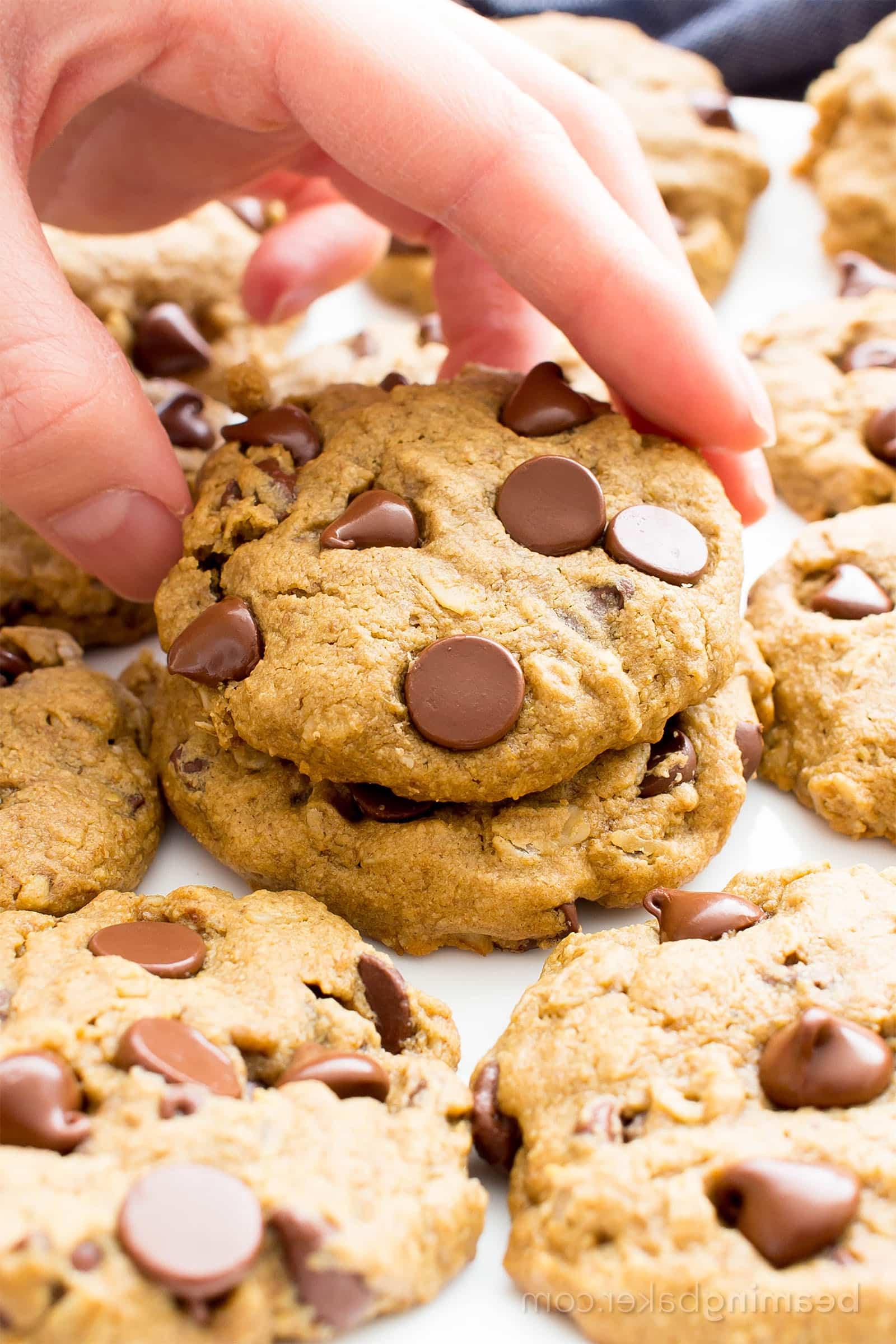 Hand picking up an oat flour cookie from plate with several more cookies on it