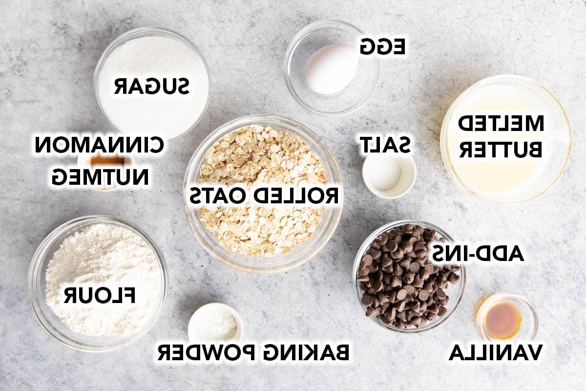 Haferflockenkeks-Schnitten 4 Die Zutaten für Haferflocken-Cookie-Riegel in vorbereiteten Schalen, darunter Haferflocken, Mehl, Zimt, Ei, Salz, Butter, Schokostückchen, Zucker, Vanilleextrakt und Backpulver.