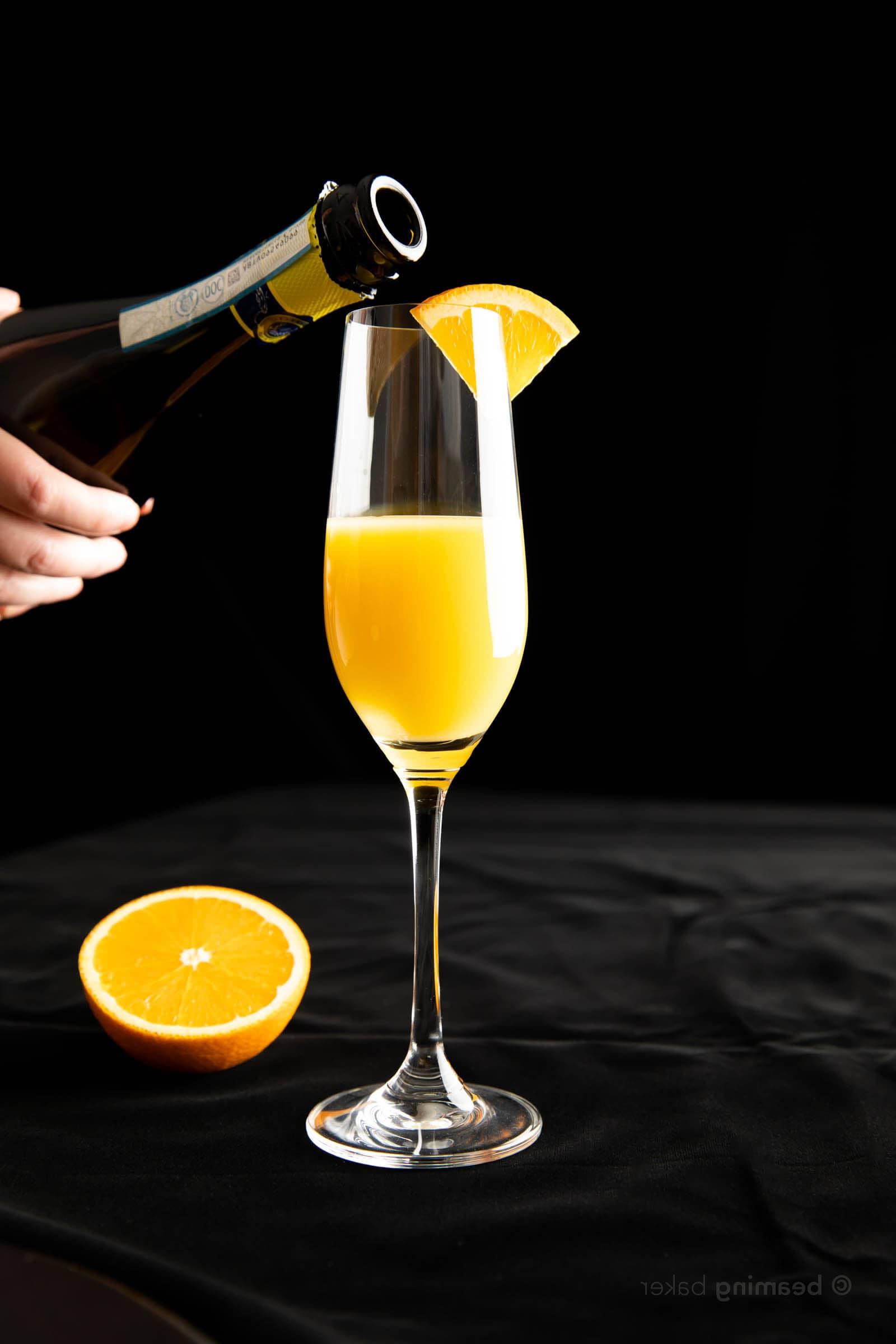 Flasche Prosecco wird über ein Sektglas gehalten, um einen Mimosa zuzubereiten