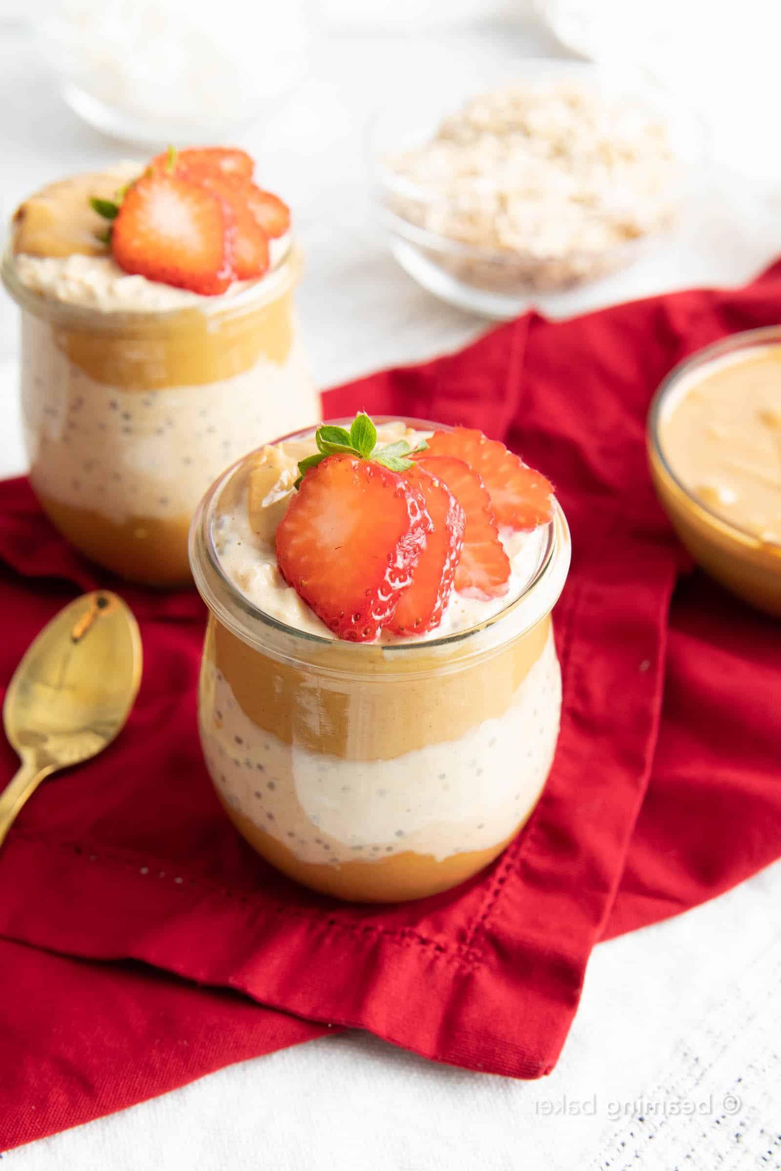 Küchentisch mit Erdnussbutter Overnight Oats in Gläsern, einer Schüssel Erdnussbutter und einer Schüssel Haferflocken