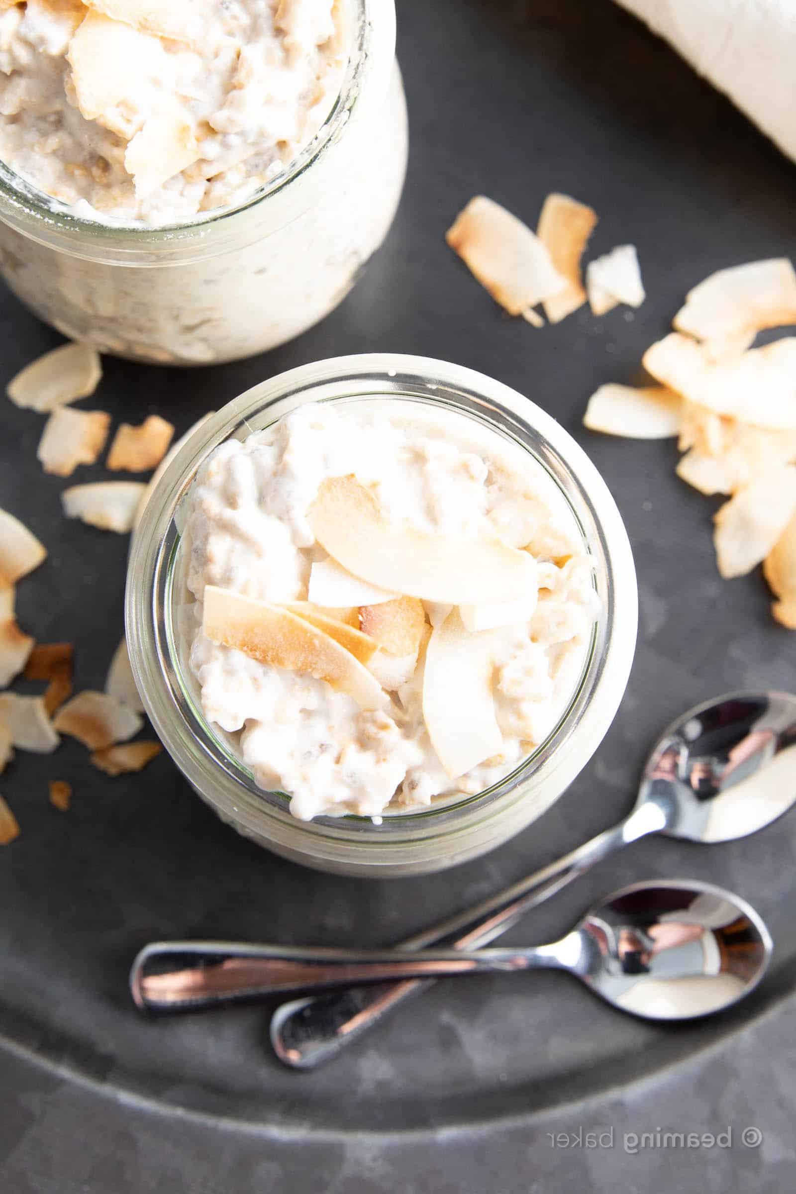 Vanille-Kokos-Overnight-Oats 5 Nahaufnahme von oben von zwei Gläsern Kokos Overnight Oats mit zwei Löffeln und passendem Geschirr