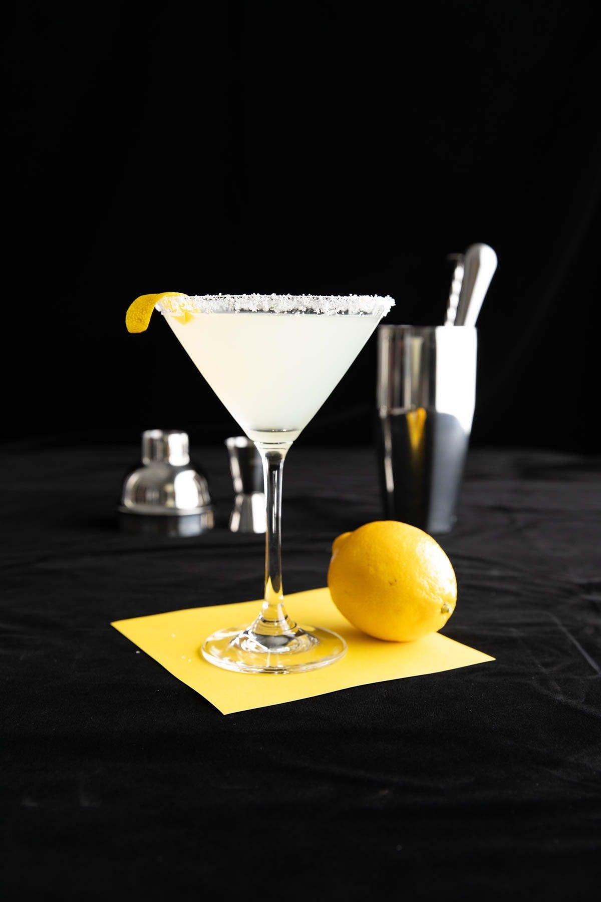 Das beste Lemon Drop Martini Rezept 6 Dieses Cocktailrezept wird in einem Cocktailglas mit Zuckerrand und einem Cocktailset im Hintergrund serviert.