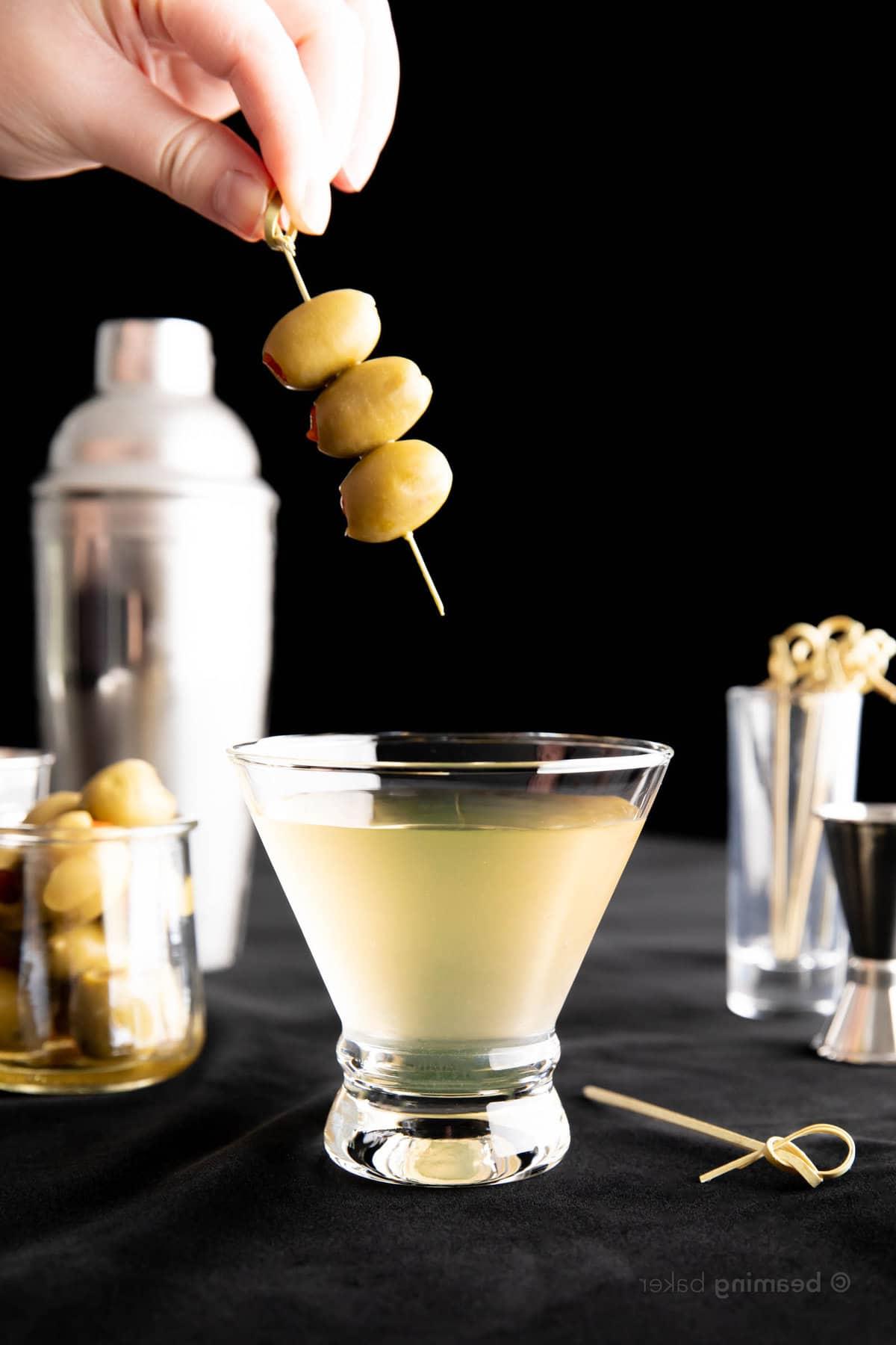 Extra Schmutziger Martini 6 Hand lässt einen Oliven-Spieß in ein kurzes Cocktailglas fallen