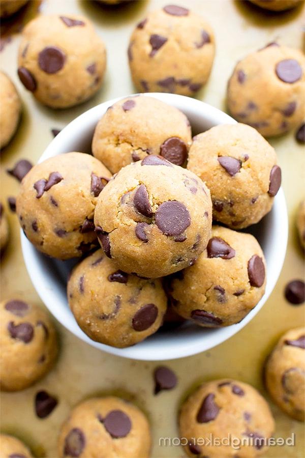 **Ungebackene Kürbis-Schokostückchen-Keksteig-Kugeln (Paleo, Vegan, Glutenfrei, Milchfrei)** 8 Kürbis-Schoko-Keksteig-Häppchen auf einem Holzbrett, mit getrockneten Blumen im Hintergrund. Eine rustikale und appetitliche Präsentation.