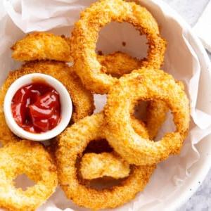**Selbstgemachte Heißluftfritteusen-Zwiebelringe** 10 Schüssel mit Zwiebelringen aus der Heißluftfritteuse, serviert mit Ketchup.