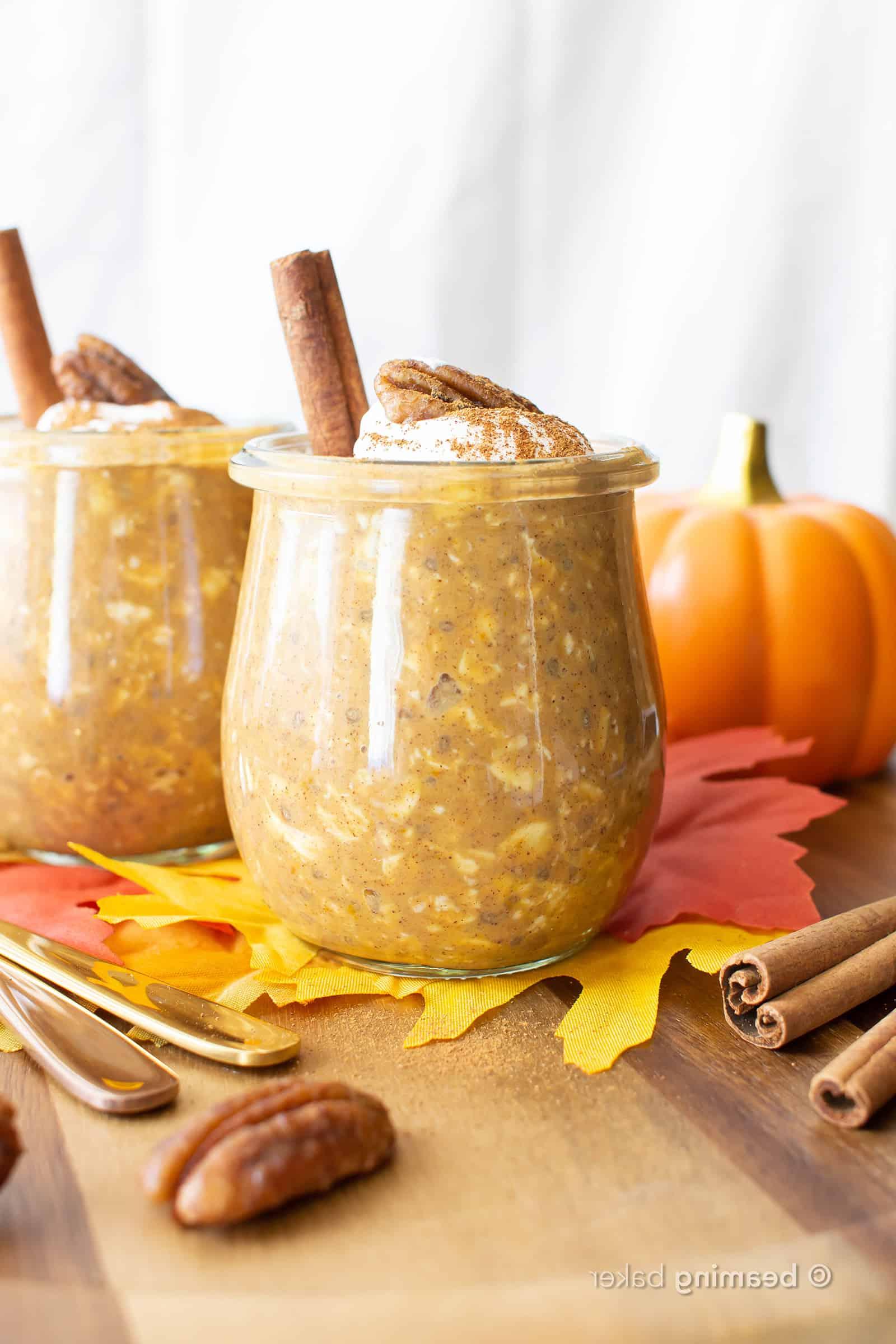 Zwei Gläser gefüllt mit Kürbis Overnight Oats, serviert mit Pekannüssen und Zimtstangen