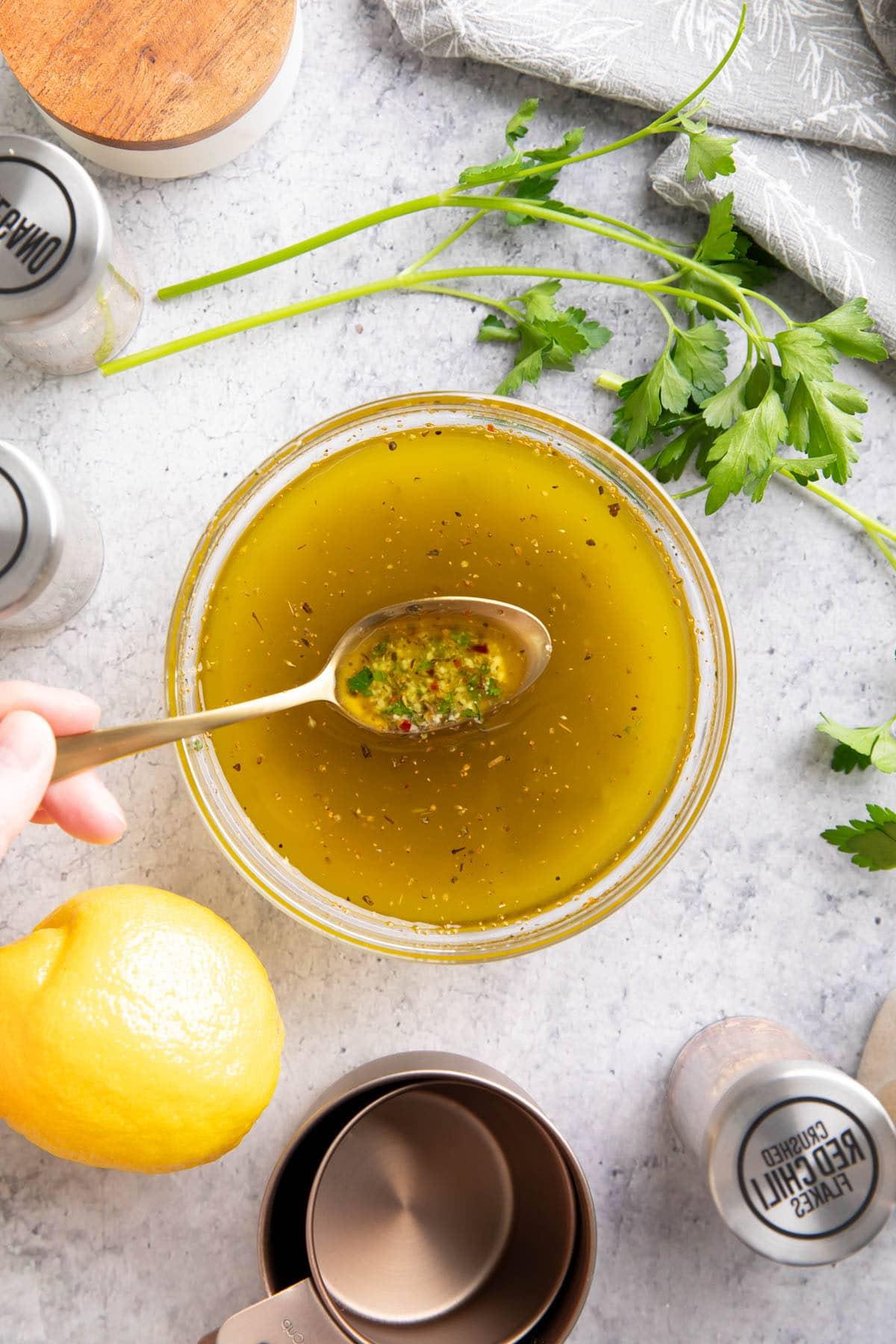 Italienisches Dressing Rezept {Einfach!} 2 Ein Löffel schöpft dieses italienische Dressing-Rezept aus einer Rührschüssel, um die Zutaten, einschließlich Kräuter, Olivenöl, Zitronensaft und mehr, zu präsentieren.