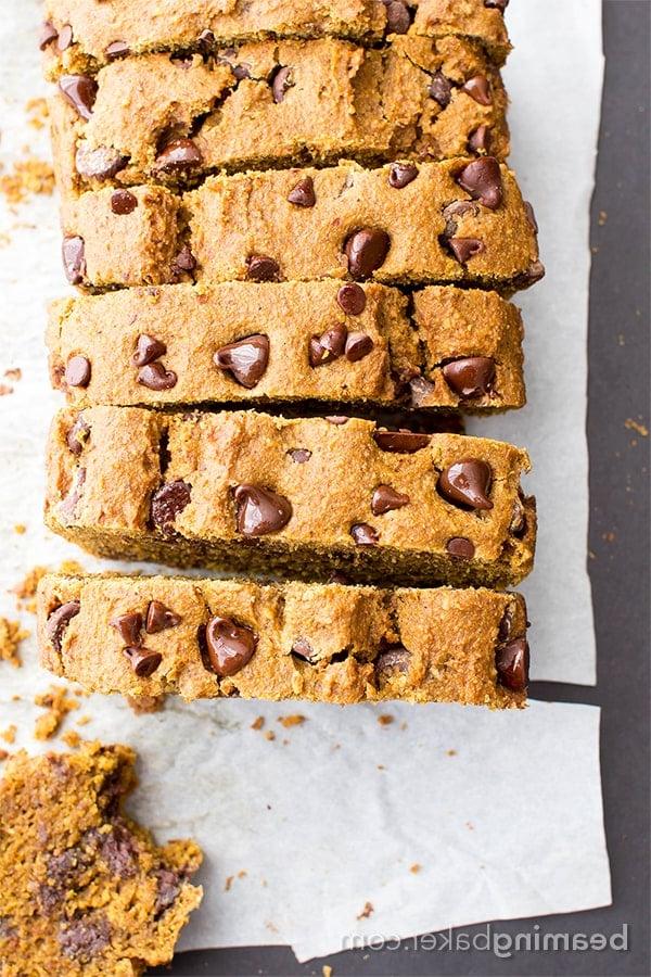 Ein frisch gebackenes veganes Kürbisbrot mit dunklen Schokostückchen auf einem Holzbrett