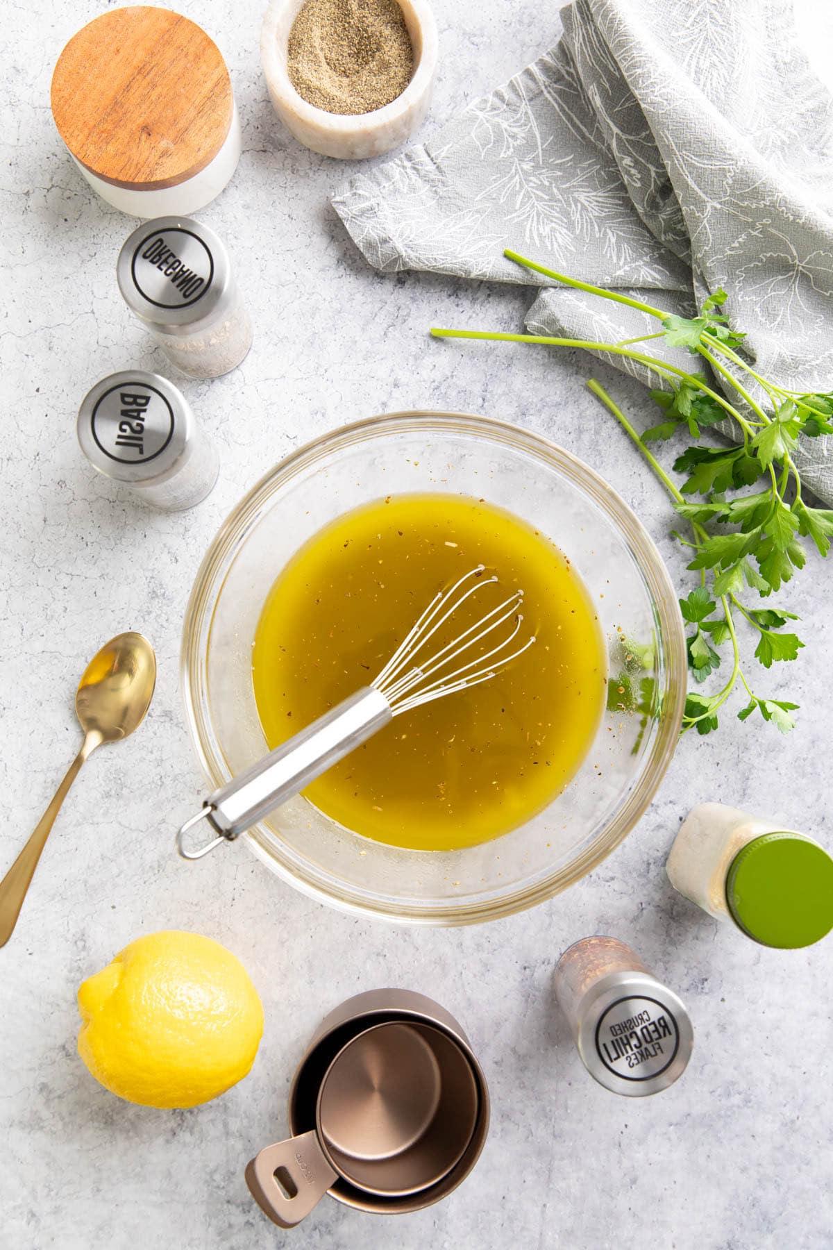 Italienisches Dressing Rezept {Einfach!} 3 Küchentisch mit Zutaten für italienisches Dressing, darunter eine Zitrone, getrockneter Basilikum, Salz, Pfeffer und rote Chiliflocken