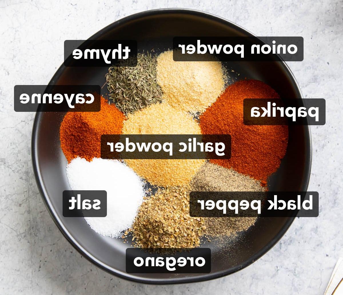Cajun-Gewürzmischung Rezept 3 Zutaten für dieses Cajun-Gewürz-Rezept, ordentlich gestapelt in einer schwarzen Schale, darunter geräuchertes Paprikapulver, Knoblauchpulver, Salz, gemahlener schwarzer Pfeffer, Zwiebelpulver, getrockneter Oregano, Cayennepfeffer und getrockneter Thymian.