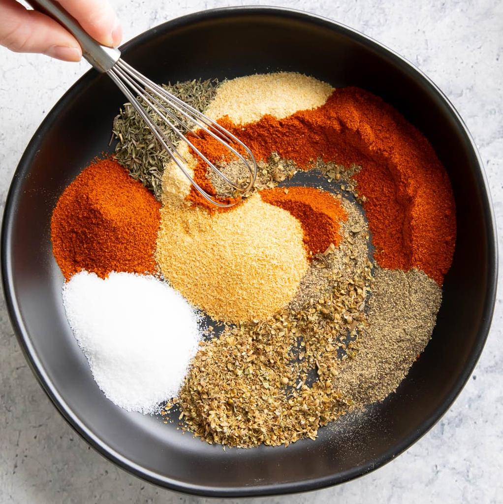 Cajun-Gewürzmischung Rezept 4 Eine Hand rührt mit einem kleinen Schneebesen in die Gewürzschale, um sie zu einer Cajun-Würzmischung zu vermischen.