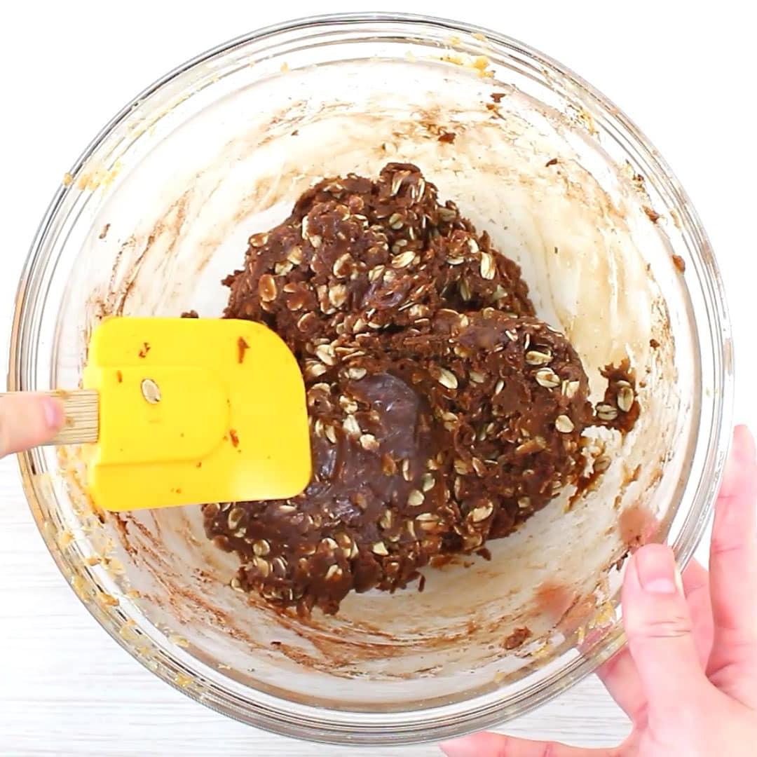 Hand hält einen Spatel, um den No Bake Schoko-Haferflocken-Keksteig fertig zu vermengen.