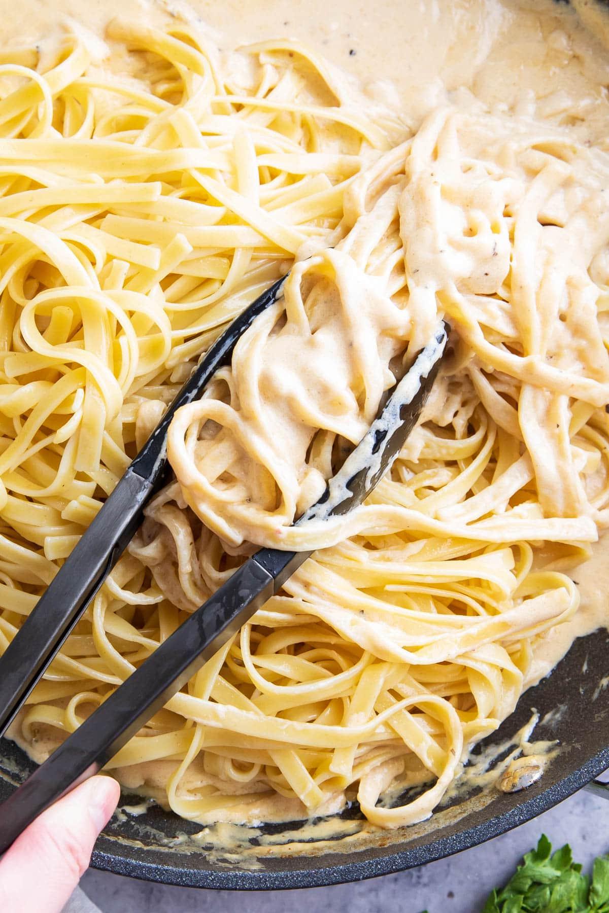Leckeres Hähnchen-Fettuccine-Alfredo-Rezept 8 Mit einer Zange al dente Pasta in der Pfanne greifen und schwenken, um sie mit cremiger Soße zu überziehen.