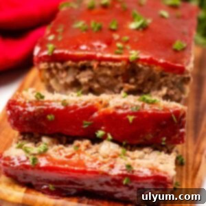 Meatloaf on a cutting board garnished with fresh parsley. Two one-inch slices are cut off the loaf.
