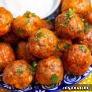Close up of buffalo turkey meatballs garnished with fresh parsley on a small plate with a small dish of ranch.