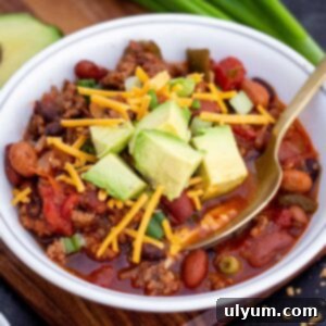 Small bowl of ground beef and sausage chili with shredded cheddar and diced avocado on top.
