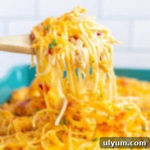 A scoop of Rotel chicken spaghetti being lifted from a baking dish with a wooden spoon, showcasing its cheesy, creamy texture.