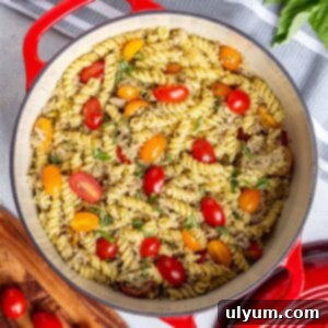 Tuna pesto pasta in a 6-quart dutch oven garnished with fresh basil. Halved cherry tomatoes are mixed in.