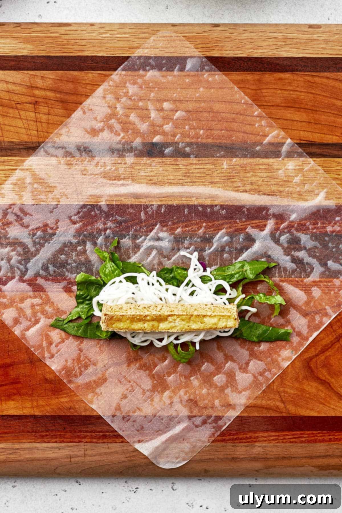 Rice paper with lettuce, noodles, and tofu laid out for rolling.