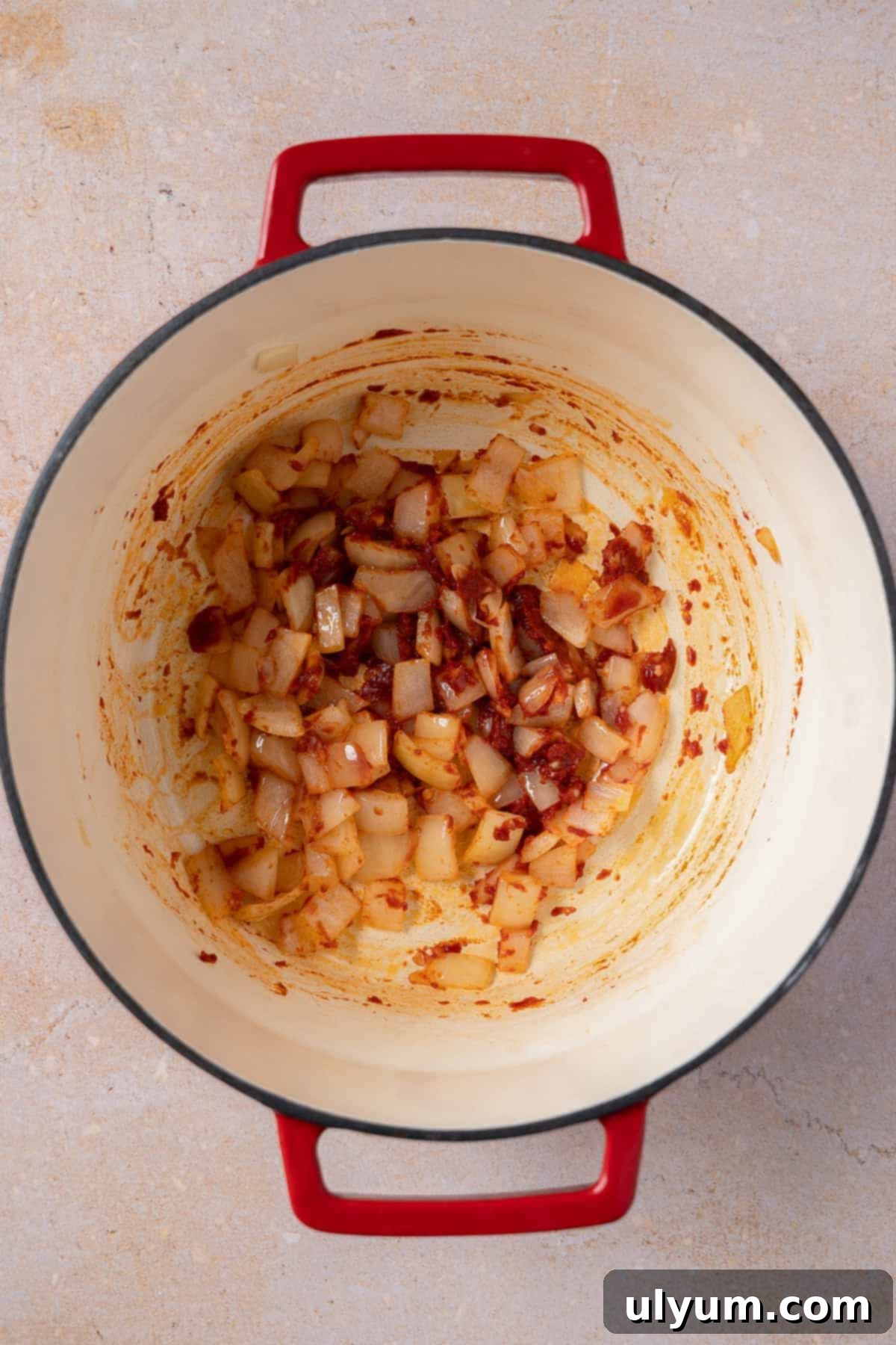 Tomato paste being stirred into sautéed onions in a pot.