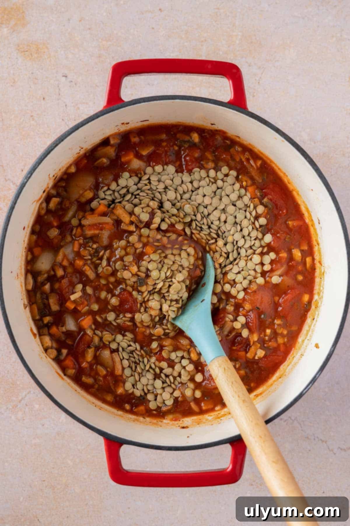 Uncooked lentils being stirred into the bolognese sauce base.
