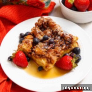 Square of French toast casserole served with berries, powdered sugar, and maple syrup.