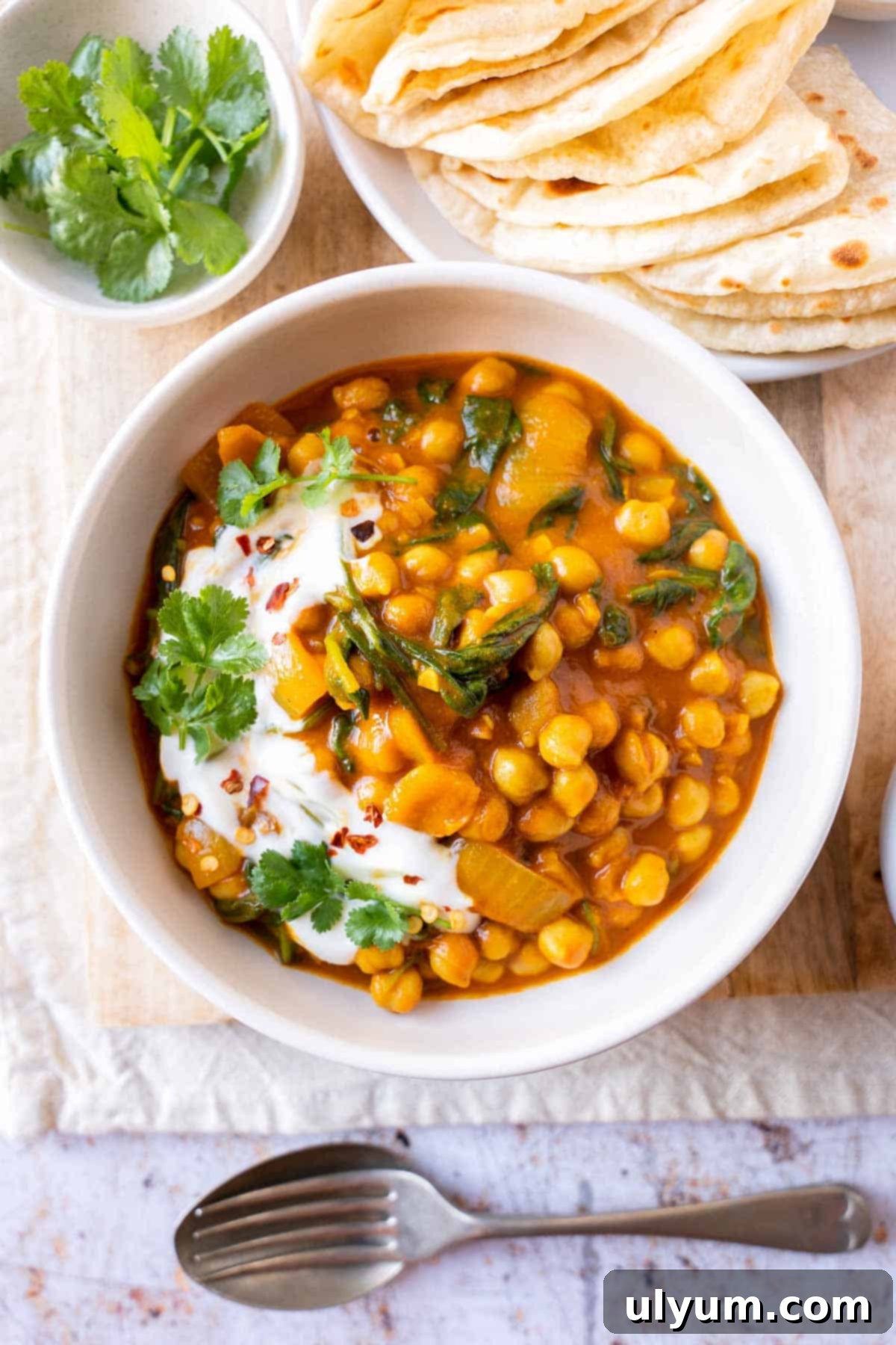 Vibrant Coconut Chickpea & Spinach Curry 2 Rich chickpea and spinach curry garnished with fresh cilantro and a dollop of yogurt, served alongside warm naan bread.