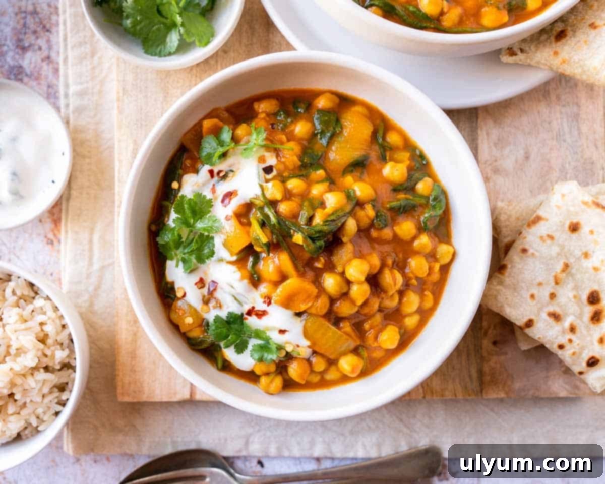 Vibrant Coconut Chickpea & Spinach Curry 13 Close-up of chickpea and spinach curry in a bowl, generously garnished with fresh cilantro and a swirl of yogurt, with a piece of naan bread in the background.