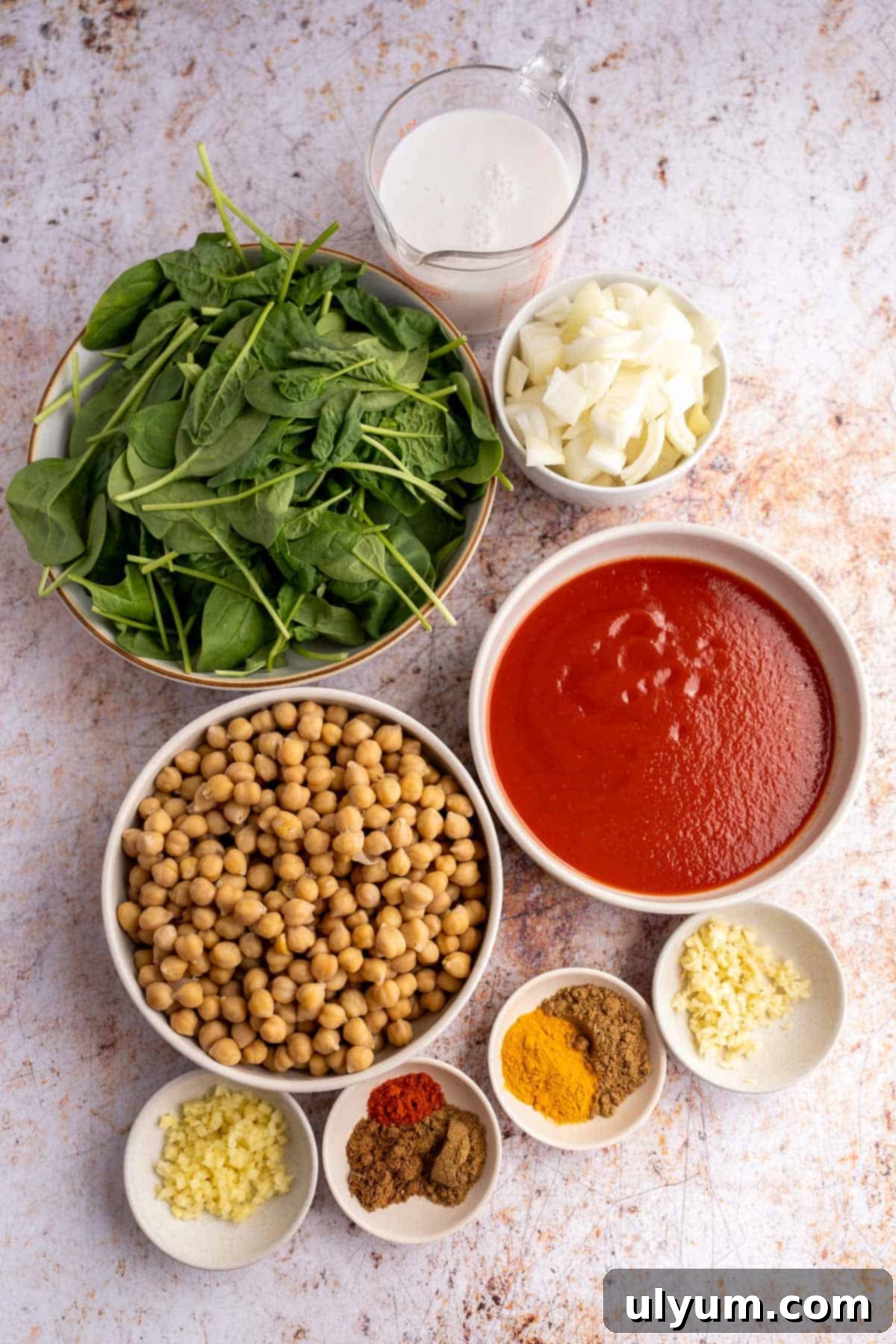 Vibrant Coconut Chickpea & Spinach Curry 3 A collection of fresh and canned ingredients for chickpea and spinach curry, including olive oil, onion, garlic, ginger, various spices, coconut milk, tomato sauce, chickpeas, and baby spinach.