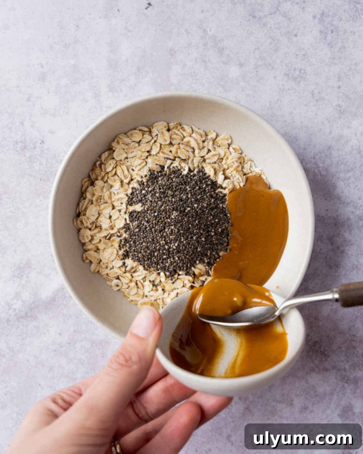 Overnight Cookie Butter Magic 5 Melted Biscoff cookie butter is poured into a bowl containing milk, oats, and chia seeds, illustrating the ingredient mixing process.