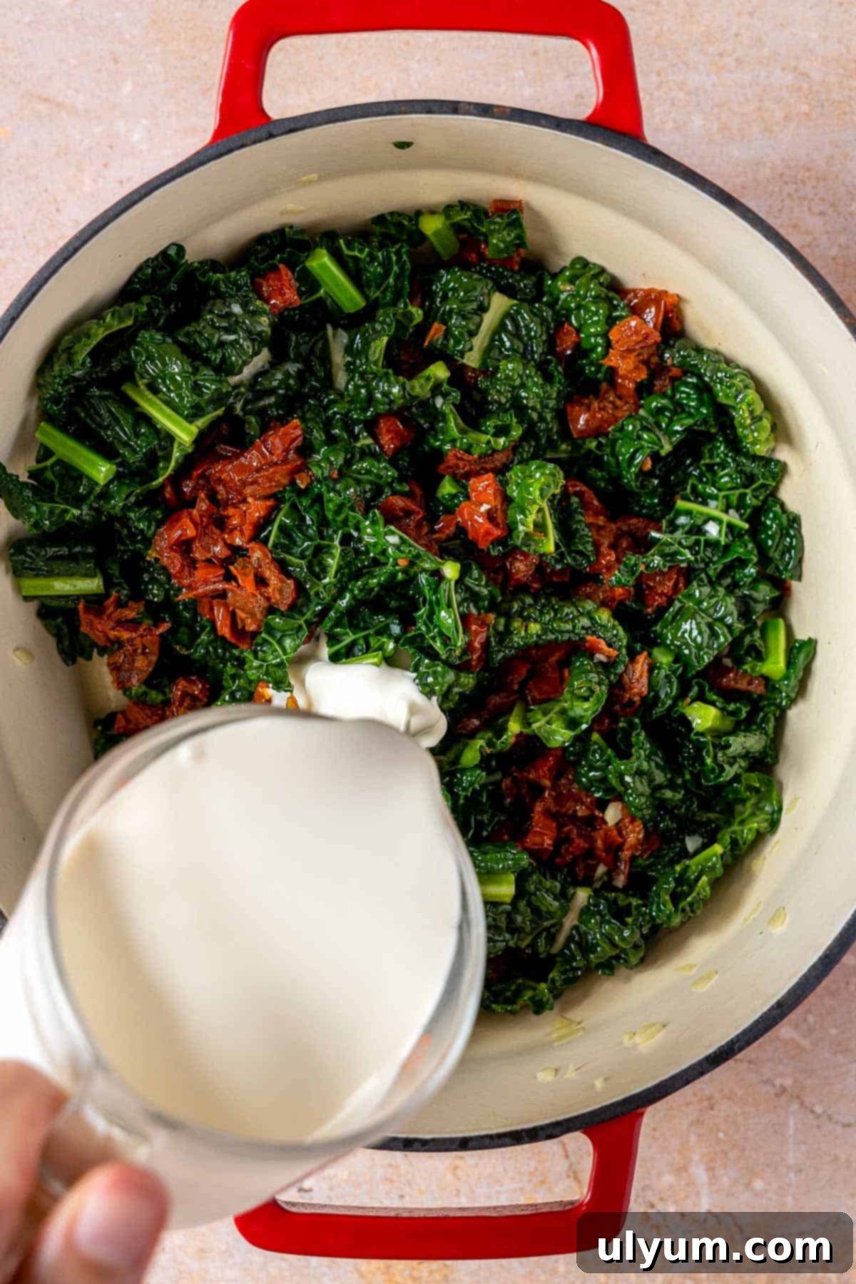 Adding heavy cream to kale and sun-dried tomatoes.