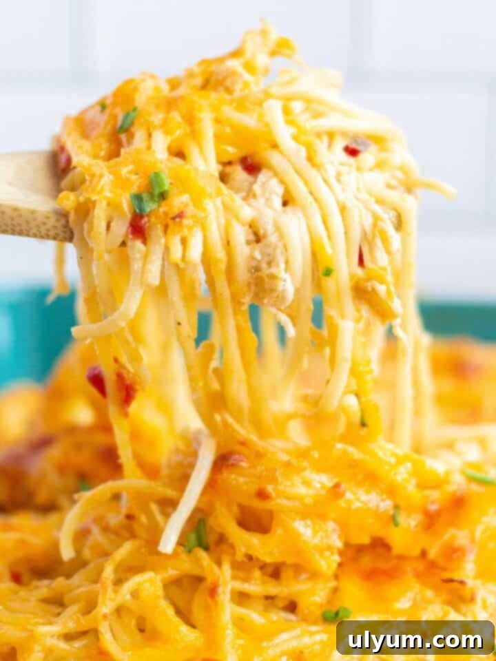 Rotel chicken spaghetti being scooped out of a baking dish by a wooden spoon.