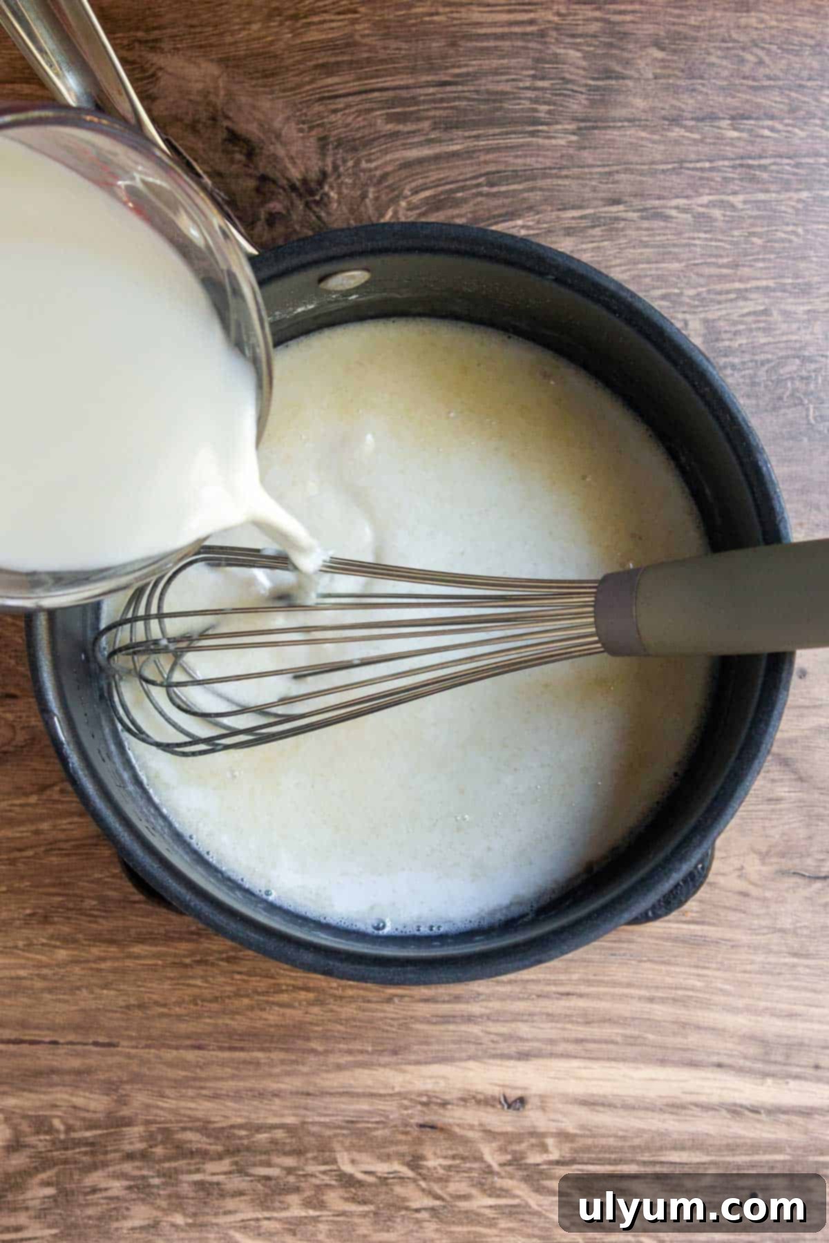 Milk slowly pouring into the flour-grease mixture, being whisked