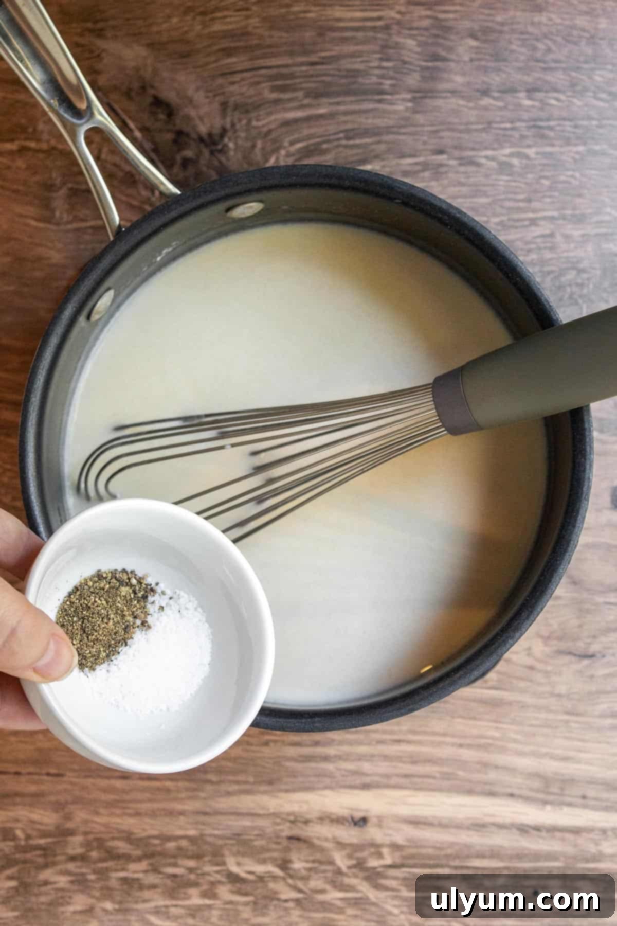 Adding salt and pepper to the white gravy mixture in a saucepan