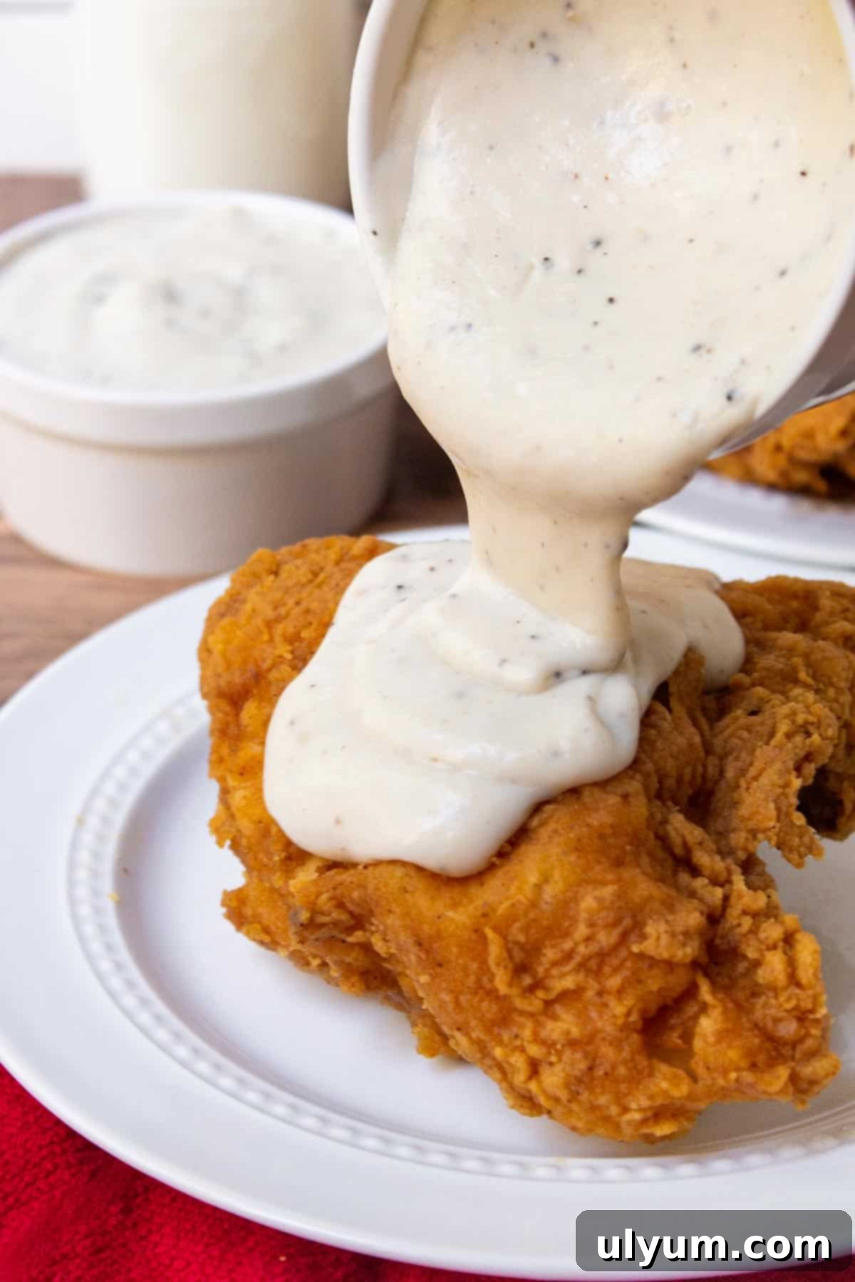 Pouring southern white gravy over crispy fried chicken pieces