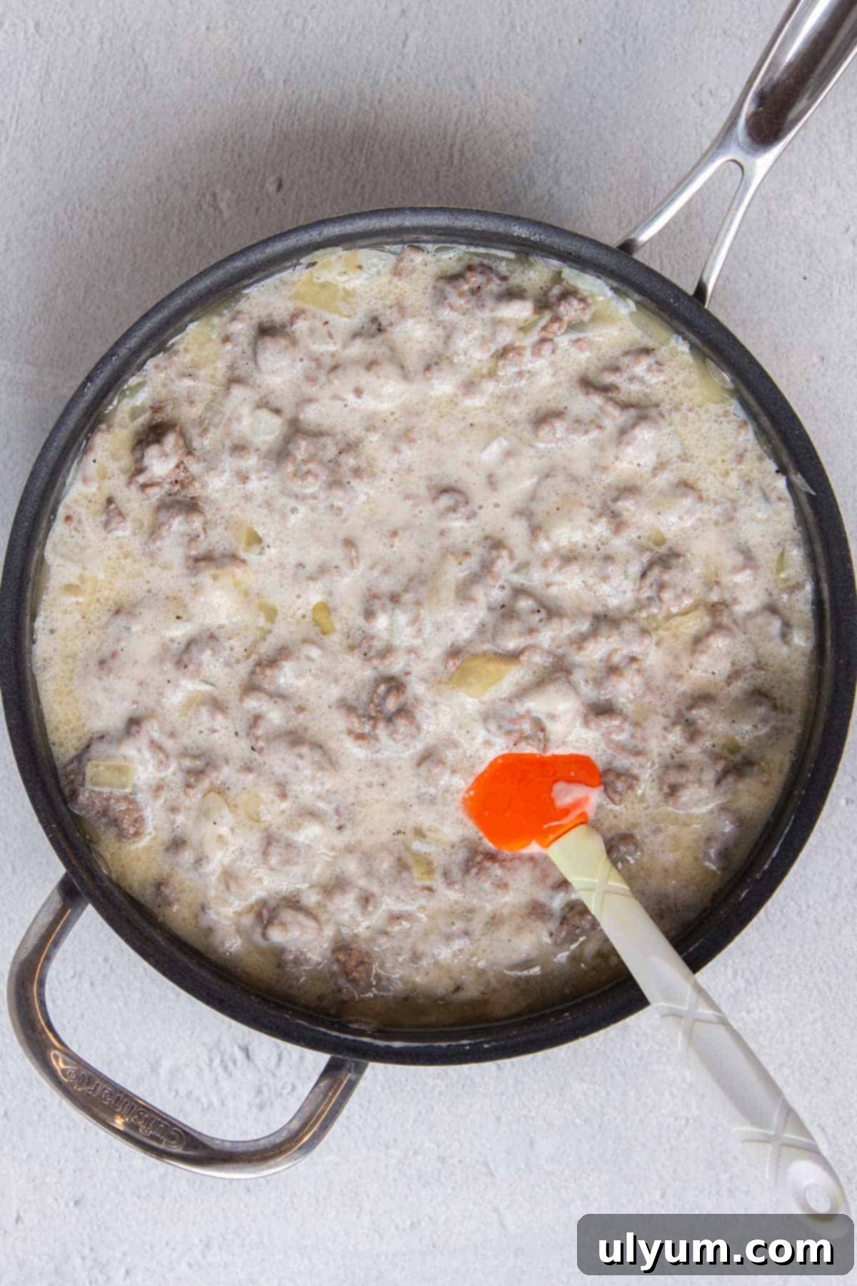 Ground beef and cream of mushroom soup mixture being stirred in a large skillet, looking creamy and well combined.
