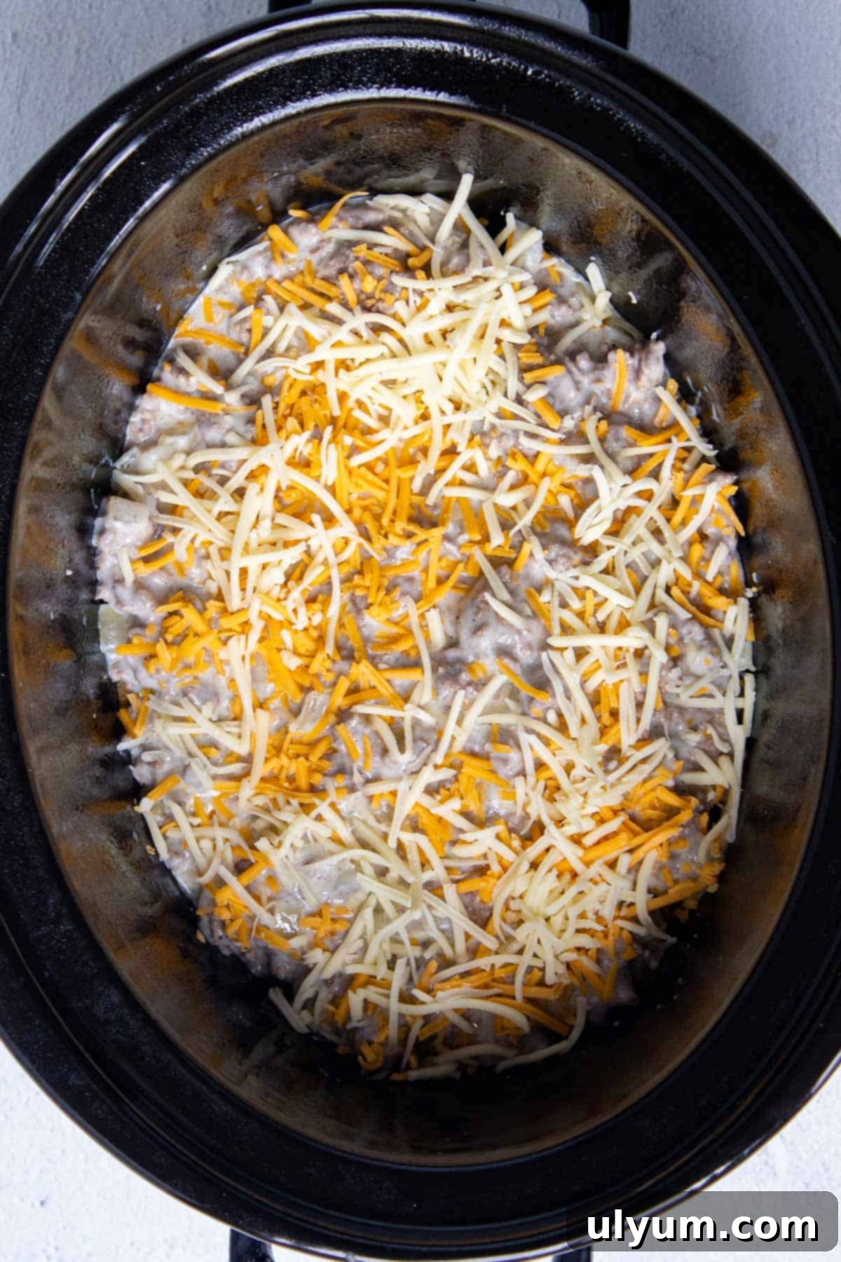 Half of the ground beef mixture and half of the shredded cheese layered over the first potato layer in a slow cooker.