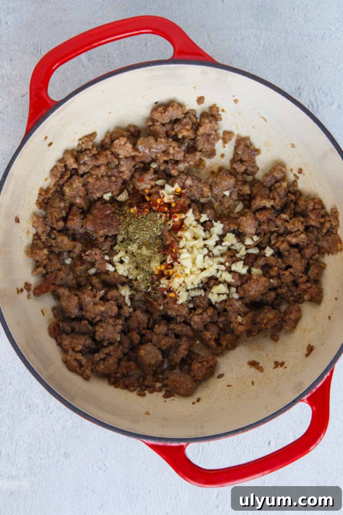Creamy One-Pot Italian Sausage Pasta 6 Garlic, Italian seasoning, and red pepper flakes mixed with cooked Italian sausage in a pot.