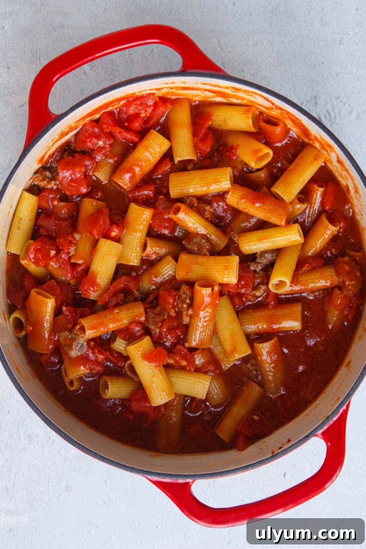 Creamy One-Pot Italian Sausage Pasta 9 Uncooked rigatoni simmering in a rich meat sauce in a large pot.