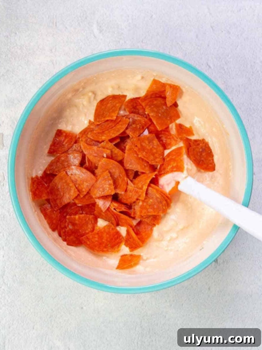 Pepperoni cut into quarters then added to the cream cheese mixture in the mixing bowl.