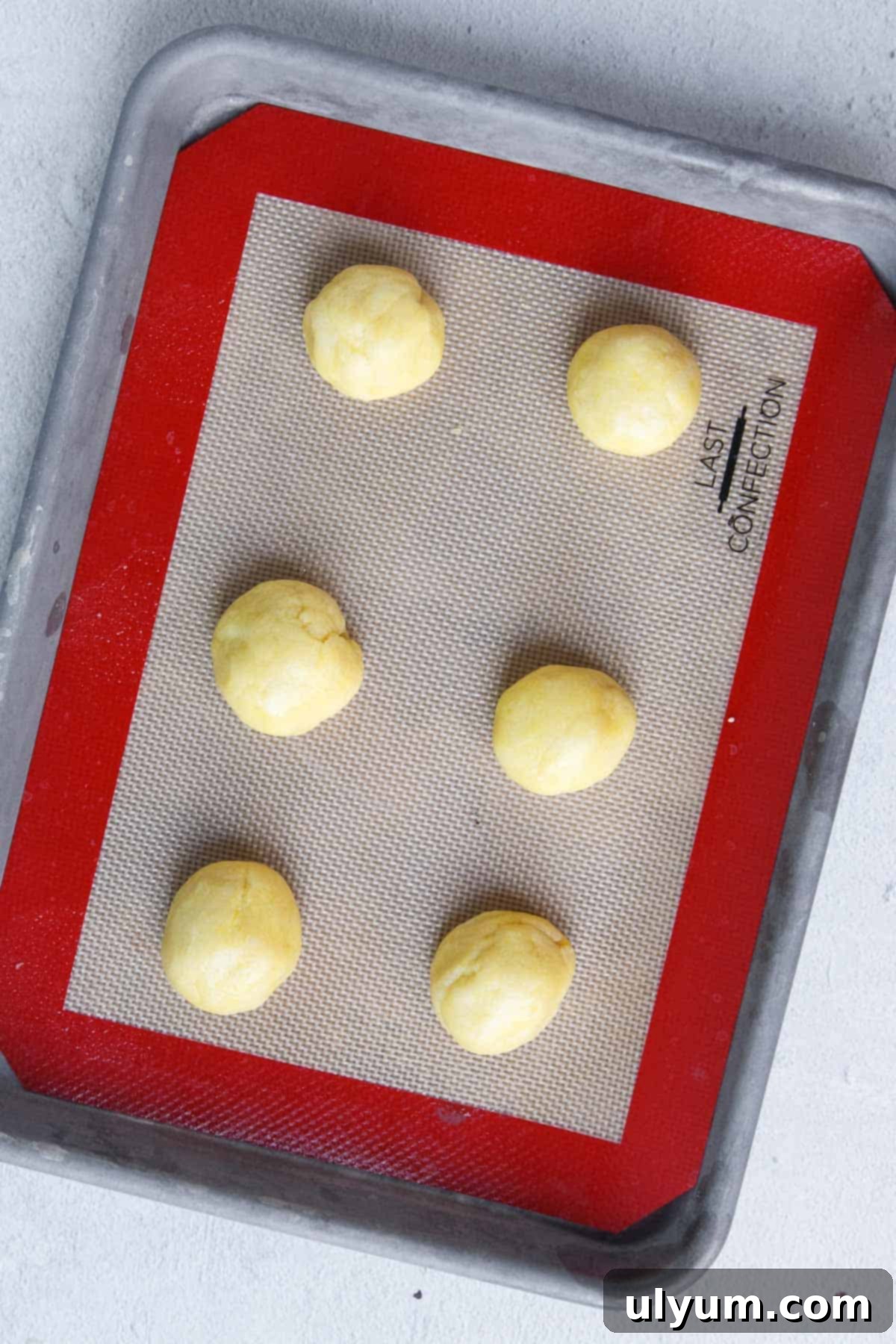 Lemon cookie dough balls on a lined baking sheet spaced apart