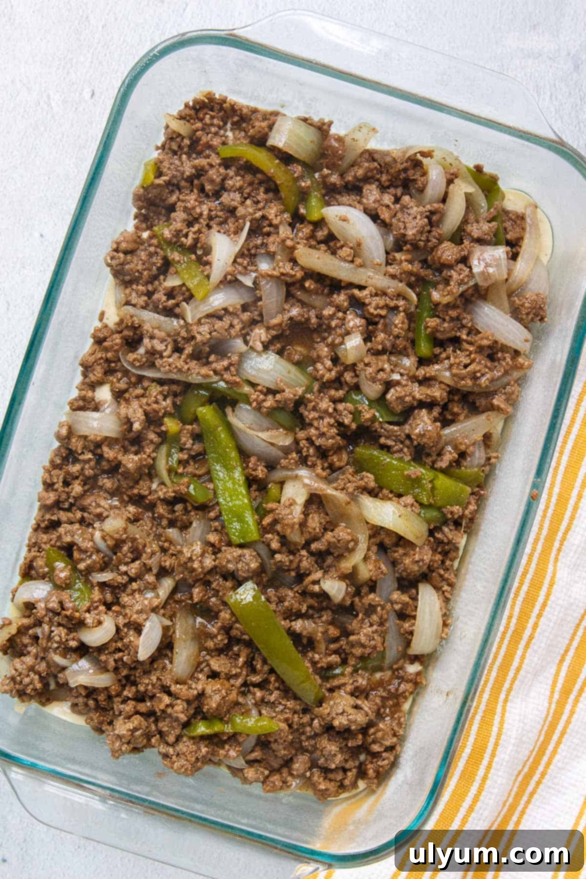 The savory ground beef mixture, loaded with onions and peppers, spread evenly over the Bisquick base in the baking dish.