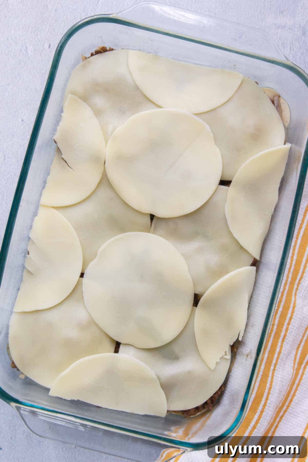 A perfectly arranged layer of provolone cheese slices covering the beef mixture in the casserole dish, ready for baking.