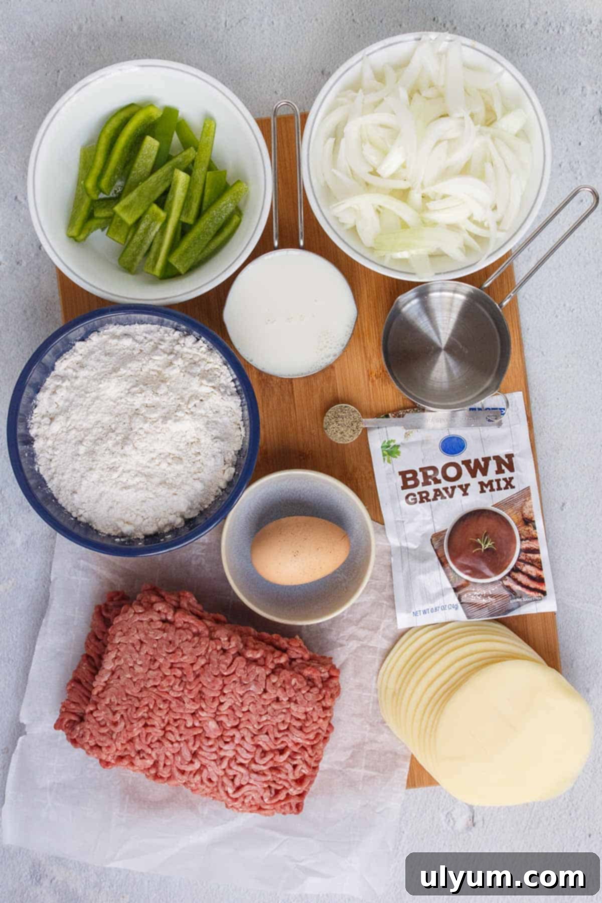 A colorful array of fresh ingredients for Philly cheesesteak casserole including Bisquick, milk, egg, ground beef, sweet onion, green bell peppers, brown gravy mix, and provolone cheese slices